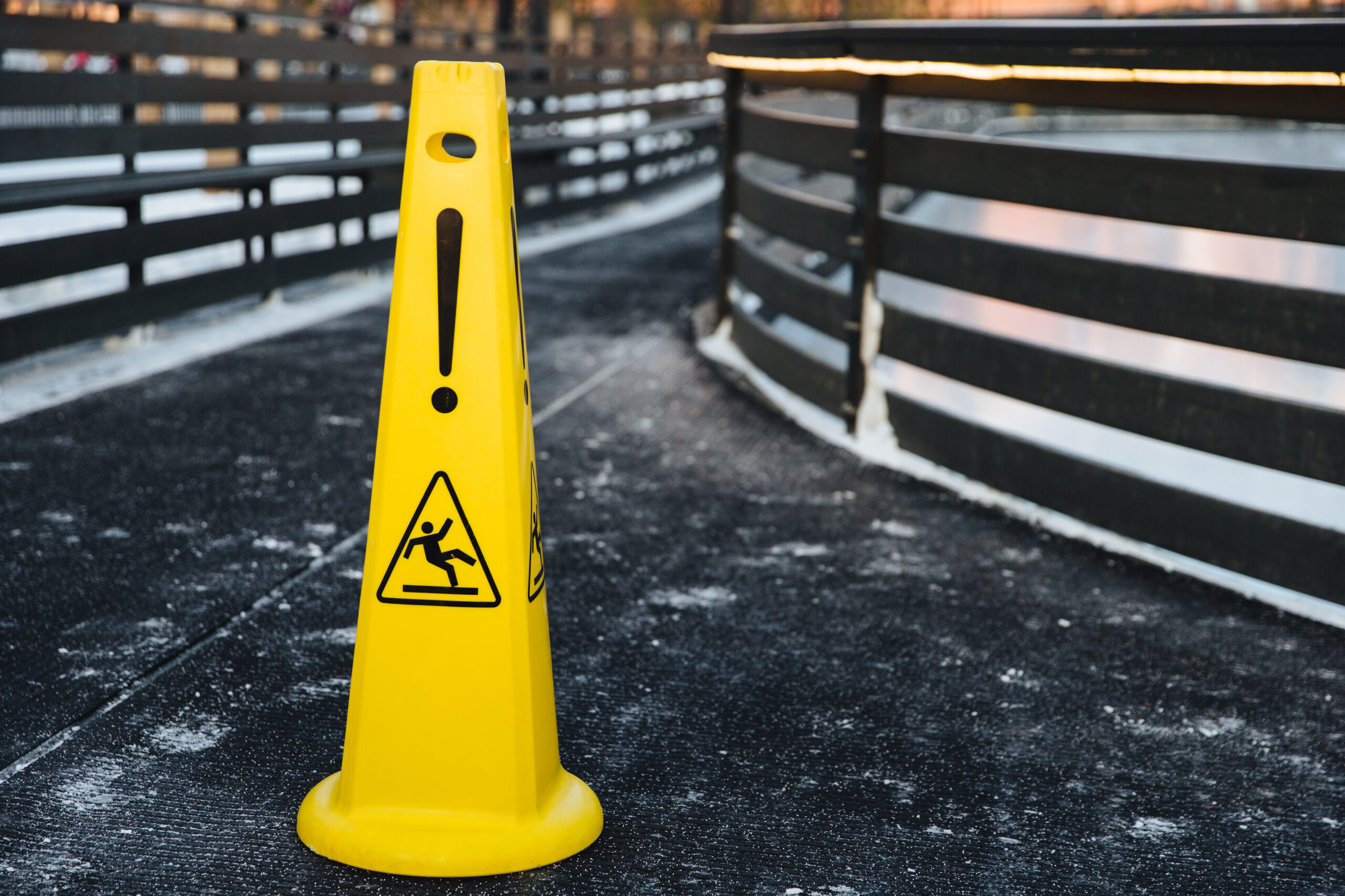 Close up shot of yellow warning sign stands on gray asphalt covered with snow, warns about wet road or slippy.