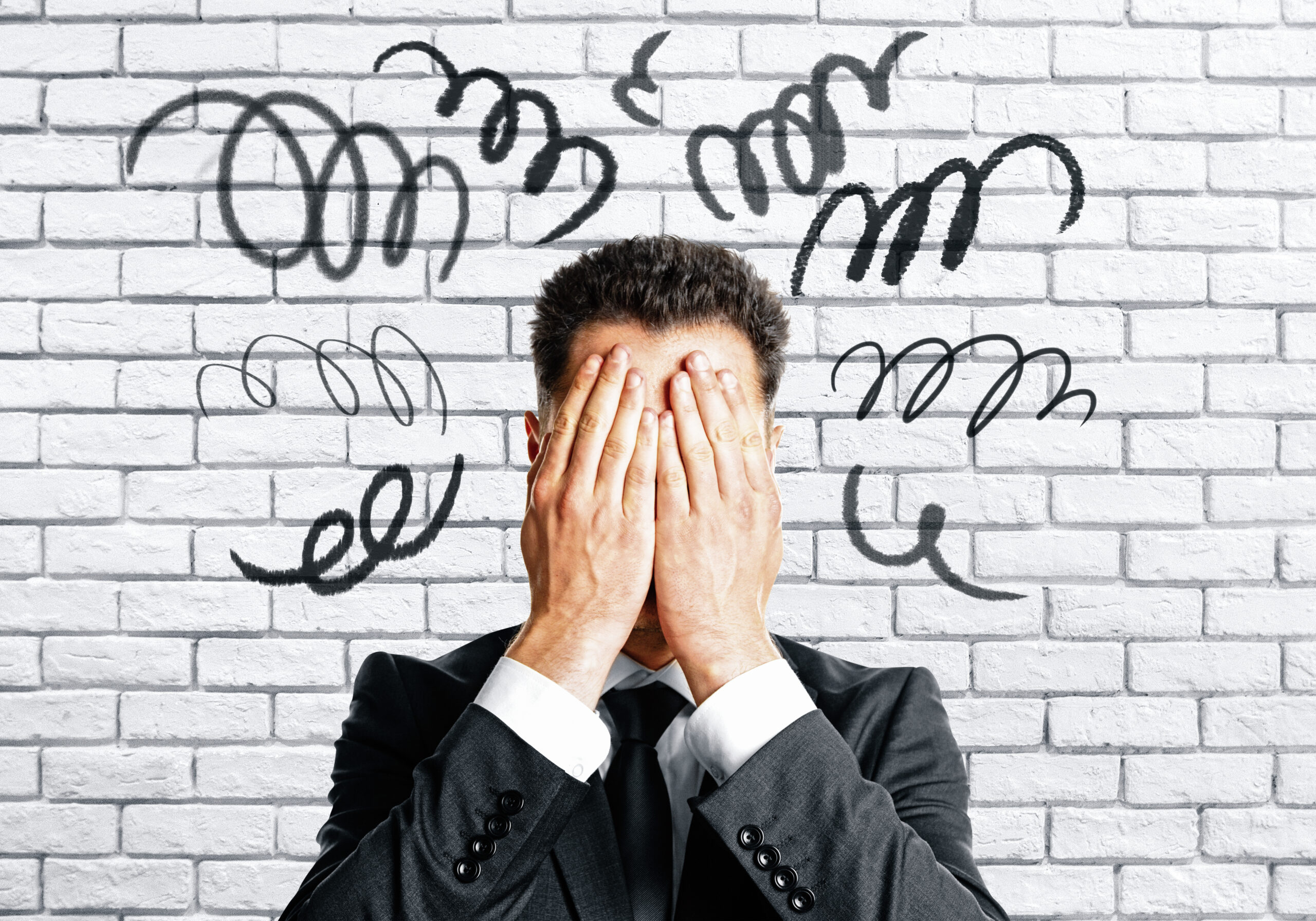 Worried businessman covering face on white brick