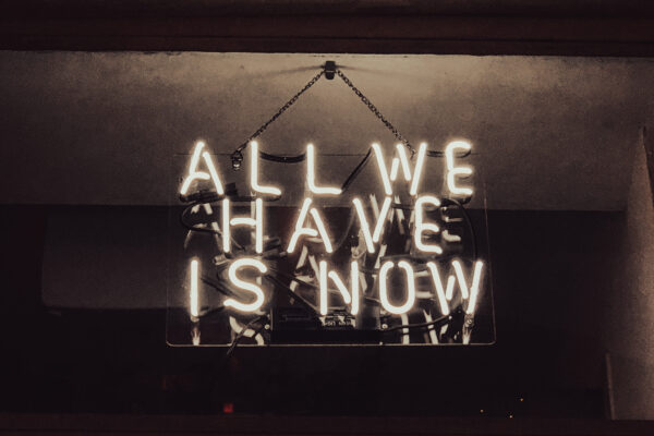 The quote "All We Have is Now" in neon lights.