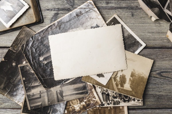 Scattered old photographs are on a wooden table with a blank card in the middle for notes.