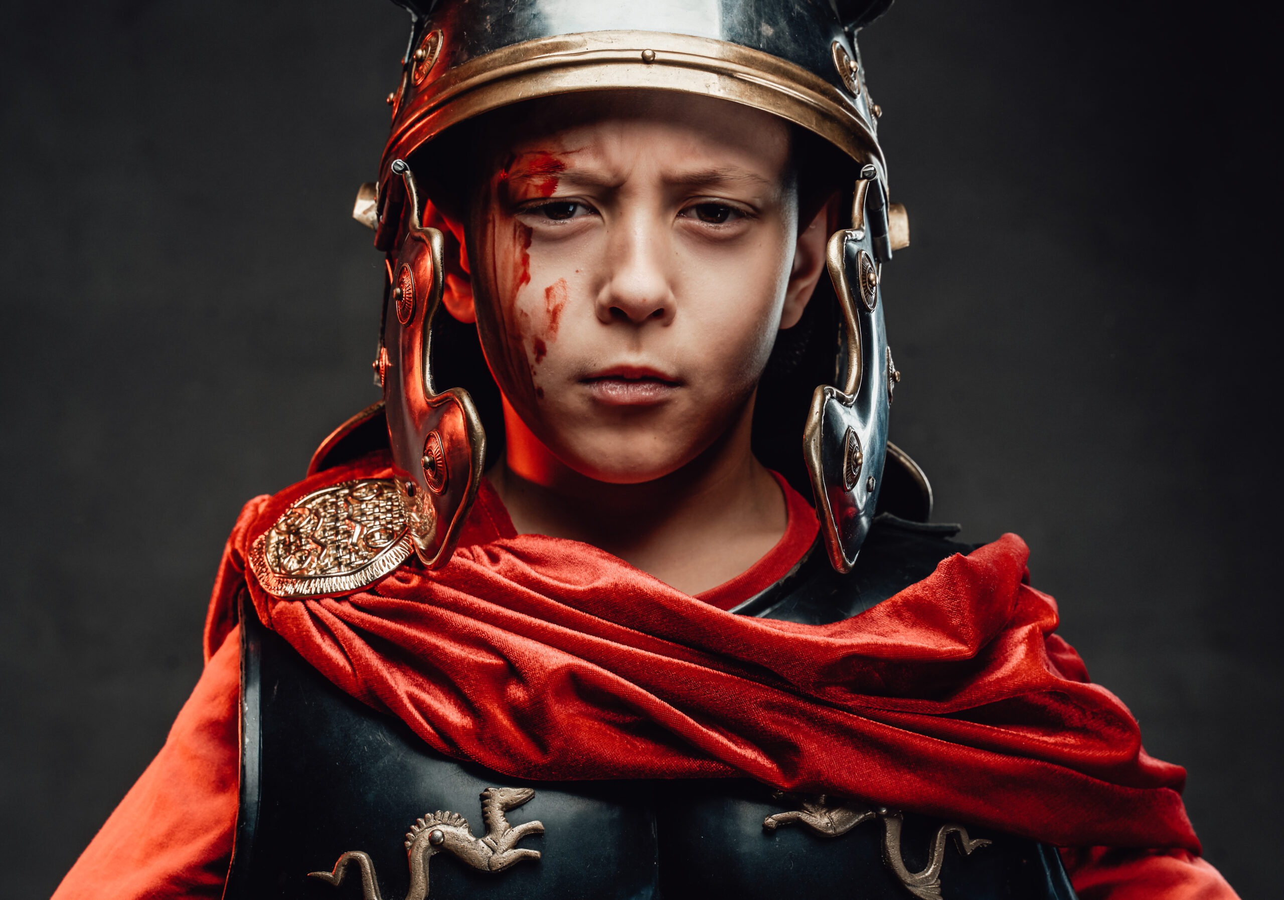 Kid dressed in dark armor with helmet and red cape.